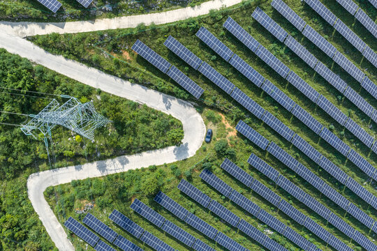Aerial View of Solar Farm on Green Slopes with Winding Road and Transmission Tower
