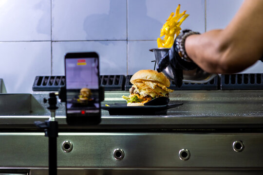 Chef recording a close-up of a stacked burger and fries for social media marketing
