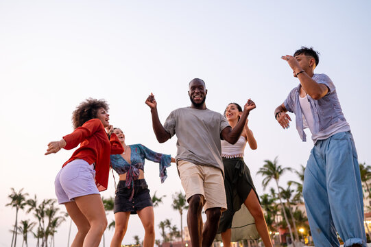 A diverse group of multicultural friends enjoying summer moments on the beach, dancing, laughing