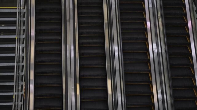 Empty metal escalators in shopping mall, dark rubber steps and stainless handrails create repeating geometric lines, moody