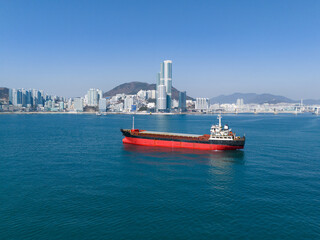 Cargo ship on blue sea with Busan city skyline in background, South Korea. Maritime transport, shipping industry and global trade concept. © soya