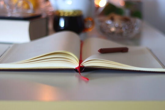 Cup of tea or coffee, teapot, book, notebook, e-reader, glasses, cookies, nuts, lemons, house plants and lit candles on the table. Hygge at home. Selective focus.