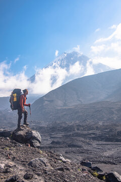 There is a man traveller on the foreground. There is Klyuchevskaya sopka on the background. The man is looking to the volcano.