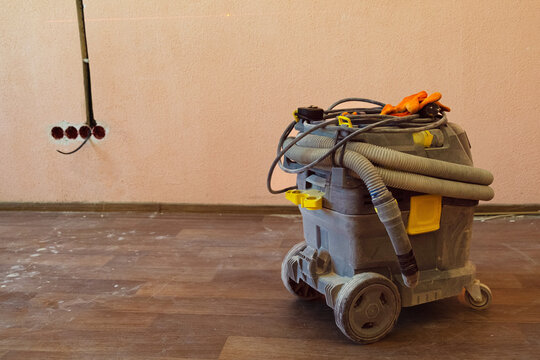 Construction vacuum in residential space during post renovation cleaning with packed debris nearby showing interior cleanup work