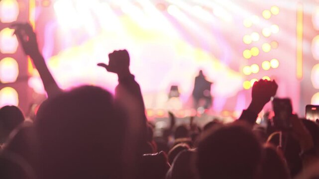 Disco. Many people dancing and jumping in rhythmic music and lights of concert or electronic music festival. Hands raised with palms up of many people on dance floor in front of stage. Entertainment