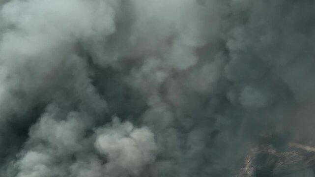 Aerial view of thick smoke rising from an industrial factory fire, spreading across the sky and reducing visibility, highlighting air pollution, environmental risks, modern industrial safety concerns.