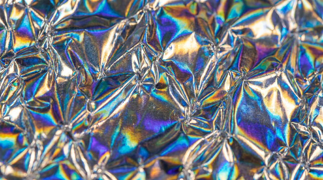 Holographic crumpled foil texture metallic iridescent shiny background abstract colorful wrinkled paper surface bright vibrant rainbow spectrum reflecting light colorful neon