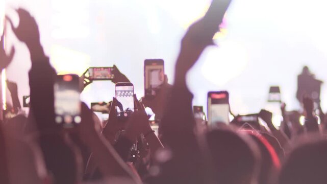 many dancing people on dance floor of concert in front of stage. Many hands using mobile phone cameras for filming disco and concert. People dance and record video. Entertainment and nightlife.