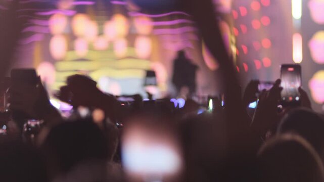 Concert spectators all use mobile phones to capture super star on stage. Raised hands holding smartphones filming disco and DJ. Concept of dance entertainment. Electronic music festival. Concert show.