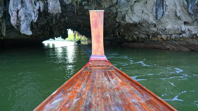 Wooden long-tail boat cruising beneath limestone formations, showcasing eco-friendly tourism, climate awareness, conservation, and harmony with natural coastal landscapes. Thailand. 4k.
