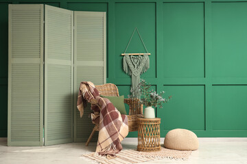 Vase with fresh eucalyptus branches on table near wicker armchair and folding screen in living room © Pixel-Shot