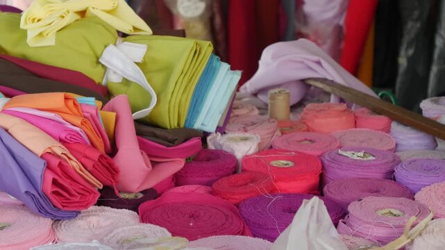 Vibrant colorful fabric bolts and textile rolls stacked at cloth market with rainbow of materials for garment making