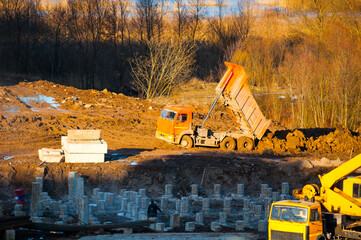 View from height of a tip truck unloading clods of soil during construction works, panel houses construction in process © syntheticmessiah