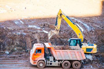 Construction site working, an excavator loads a tip truck with soil during construction works, panel houses construction in process © syntheticmessiah
