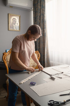 Woman sewing decorative trim on fabric at home craft table in a sunlit room