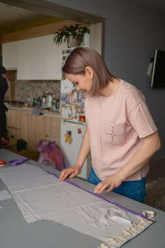 Woman measuring fabric for sewing project at home kitchen table, concentrating on dressmaking details