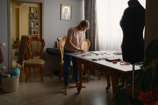 Woman sewing and cutting patterns at a home workspace with mannequin and ornate chairs