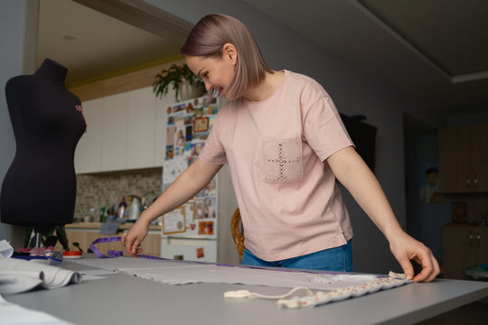 Woman measuring fabric on a worktable while sewing with a dress form in a home studio