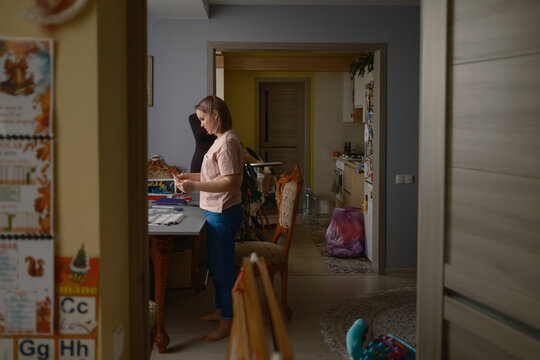 Woman sewing and crafting at a home table near a dress form in a lived-in apartment interior