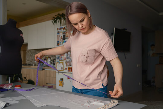 Woman measuring fabric for sewing project in a home studio with dress form and tools