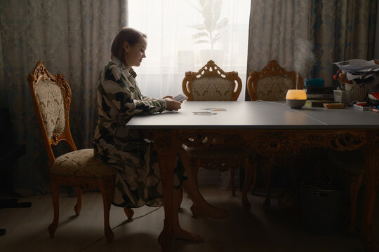 Woman reading tarot cards at ornate dining table with diffuser and vintage chairs in soft light