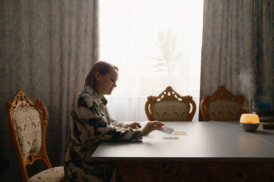 Woman doing a quiet tarot card reading at a table with warm diffuser light and vintage chairs
