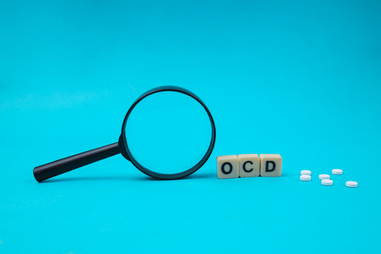 Close Up Of Magnifying Glass Near OCD Word Tiles And White Pills For Mental Health Concept