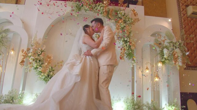 A joyful bride and groom sharing a romantic kiss on a beautifully decorated stage during their wedding celebration.