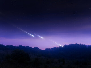 Meteorites in the sky at dawn. Fireballs over the hills. Meteor trails over the horizon. Astronomical landscape. © Nazarii