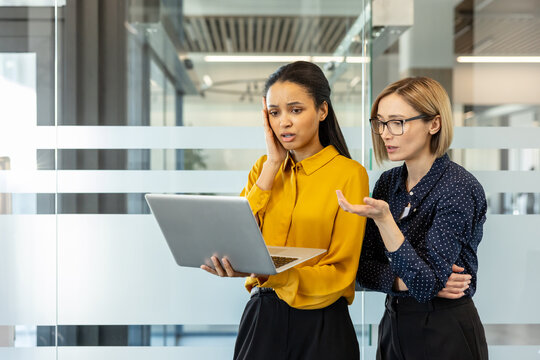 Colleagues discussing a digital issue on a laptop, showing concern and confusion while trying to find a solution to a technical difficulty in an modern office environment