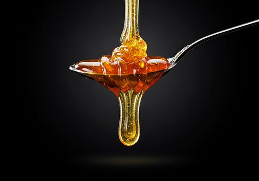 Golden honey syrup dripping from a metal spoon on dark background with smooth flow