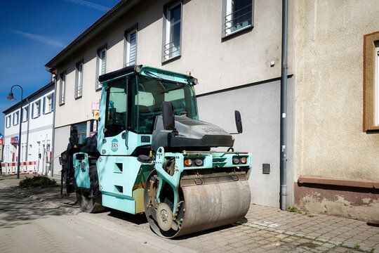Eine t&uuml;rkisfarbene schemelgelenkte Tandemwalze der Marke BOMAG Modell BW 154 AC am Strassenrand vor einem Haus geparkt
