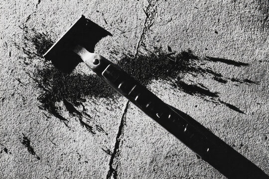 Trans man shaving face with safety razor on textured concrete surface, dramatic shadow and scattered hair create bold and emotional atmosphere