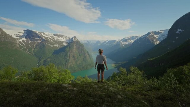 A sporty woman walks toward a stunning viewpoint over Oldevatnet in Norway on the Klovane hike. Snow-capped peaks and turquoise water create a breathtaking alpine scene.