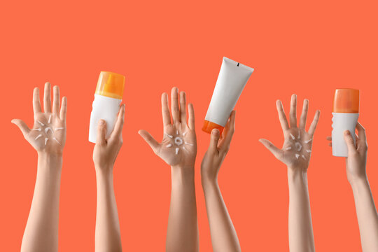 Female hands with sun made of cream and bottles of sunscreen on orange background