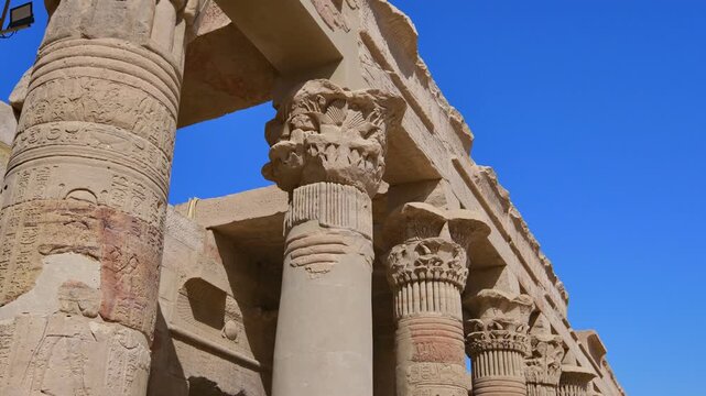 Looking up through carved sandstone columns with decorative papyrus capitals and stone crossbeams at Philae temple, Aswan, Egypt, clear blue sky above.