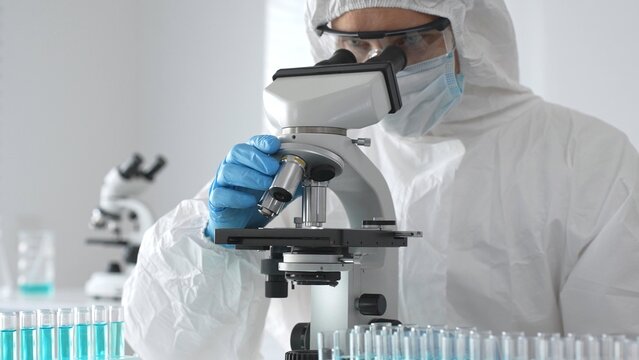 Medical virologist in protective hazmat gear examining viral samples under a microscope while conducting research in a sterile laboratory environment