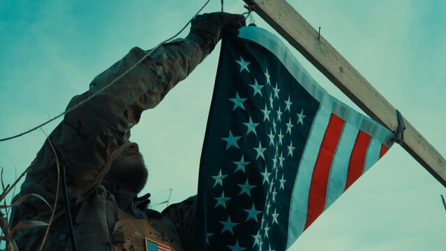 A soldier sets up an American flag at a makeshift base in desert Memorial day