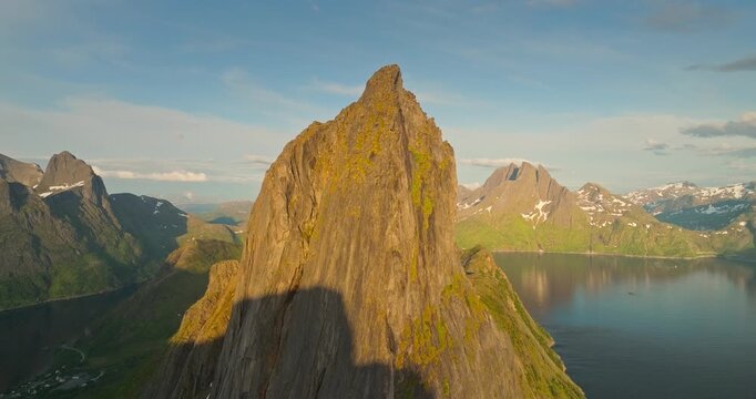 Close-up drone view of Segla peak on Senja island during midnight sun. Snow-capped mountains reflect in calm water, captured from the Hesten hike in a stunning Arctic landscape.