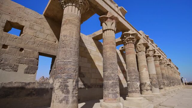 Low angle upward view of ornate papyrus capital columns and stone architrave against vivid blue sky inside ancient Egyptian Karnak or Philae temple, Luxor or Aswan, Egypt.