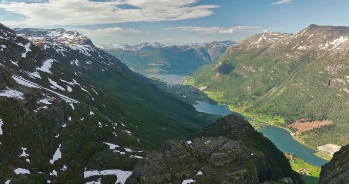 Drone flies over a mountain peak revealing turquoise waters of Oldevatnet, surrounded by snow-capped mountains. Stunning Norwegian alpine scenery with vivid colors.