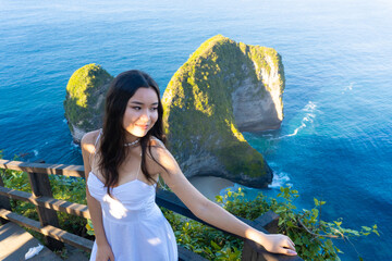Young woman in white dress posing at Kelingking Beach on Nusa Penida, Bali, with iconic cliffs and ocean backdrop. © DR26