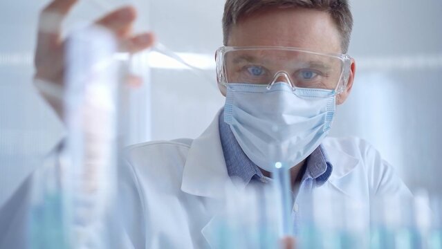 Man with safety glasses and blue mask is working with lab tubes
