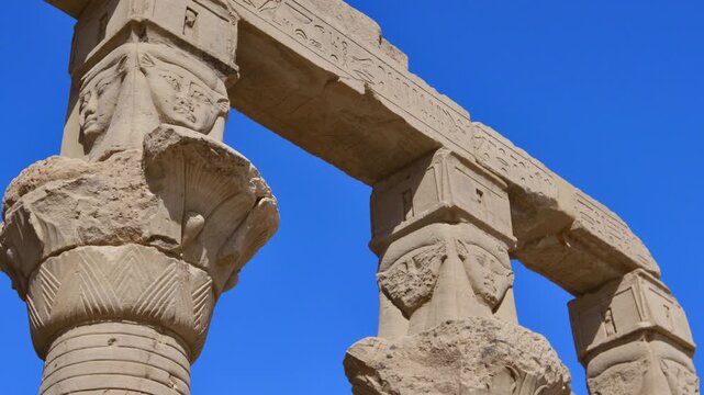 Ancient Egyptian Hathor columns with carved deity faces at Philae temple on Agilkia Island, Aswan, Egypt, stone architrave with hieroglyphics above.