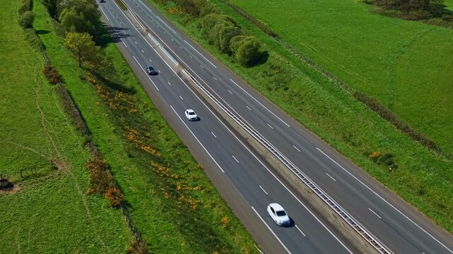 Dual carriageway likely N162 road in Mayenne department Pays de la Loire region France with car traffic through bocage farmland landscape, drone slow oblique glide shot