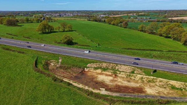 Dual carriageway road with car traffic in Mayenne department Pays de la Loire region France crossing bocage farmland landscape, drone forward approach oblique aerial shot