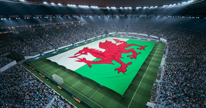 Professional Stadium Soccer Game Championship With Flag of Wales Spread Across the Pitch Before Football Match Start. Cheering Crowds of Fans Surround the Field. Aerial Wide Shot
