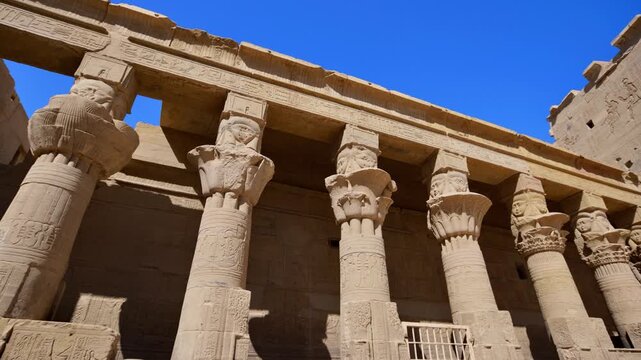 Iconic Ptolemaic columns with Hathor face capitals and floral carvings at Philae island temple, Aswan, Egypt, hieroglyphic inscriptions on architrave above.