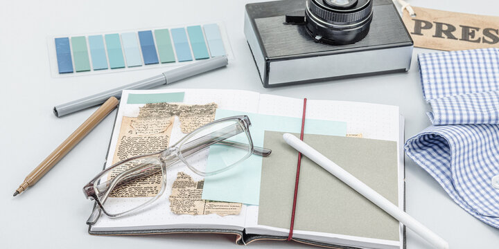 Flat lay of retro journalist essentials on blue background: camera, press badge, notebook