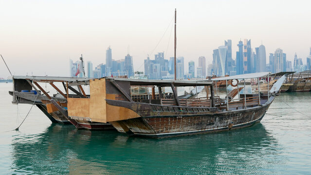 Traditional wooden dhow boat on turquoise water with Doha skyline in the background, Qatar